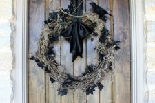 a scary Halloween wreath of vine with moss and black leaves, a faux black bird and a black ribbon is a chic idea you can try
