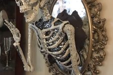 a scary glam Halloween decoration of a vintage mirror with a glam embellished half skeleton attached is elegant