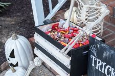 a skeleton in a hat holding a crate with sweets and chocolate is a great idea for kids that will come for treat or trick