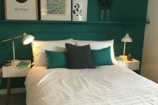 a small and bright bedroom with an emerald accent wall, a matching bed and pillows, small white nightstands with table lamps and a ledge with art