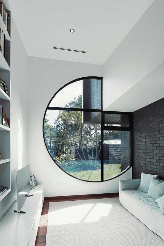 a small minimalist living room in white with a large porthole window partly integrated into the wall