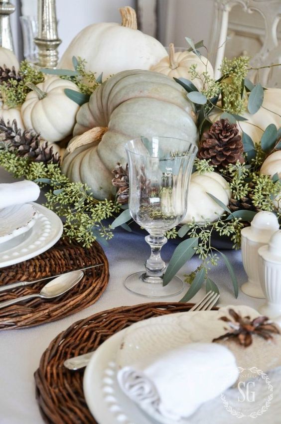 a soft and natural Thanksgiving tablescape with woden placemats, white plates and neutral pumpkins, greenery and pinecones is amazing