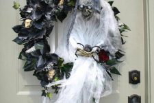 a spooky Halloween wreath of black faux blooms and leaves, skulls, a ghost with a bloom is jaw-dropping