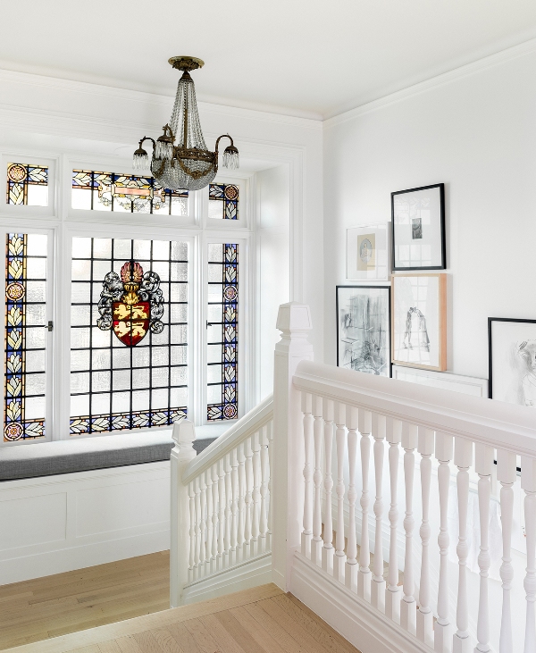 a staircase with a large window with stained glass and a built in windowsill seating plus a gallery wall and a chic chandelier