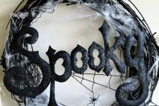 a stylish and scary black Halloween wreath of vine, spiderweb, spiders, glitter letters and a silk ribbon bow is pure chic