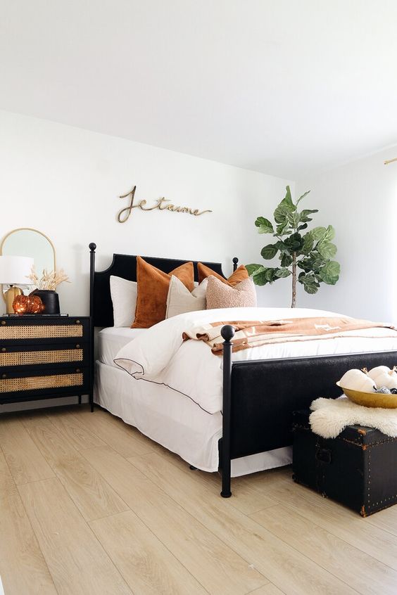 a stylish bedroom with a black bed, a black dresser, a black chest that doubles as a bench, pumpkins in a bowl and wheat in a vase