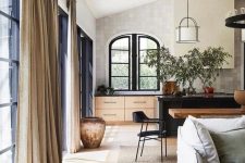 a stylish contemporary interior with black framed arched windows, a black kitchen island and black chairs, neutral drapes and furniture