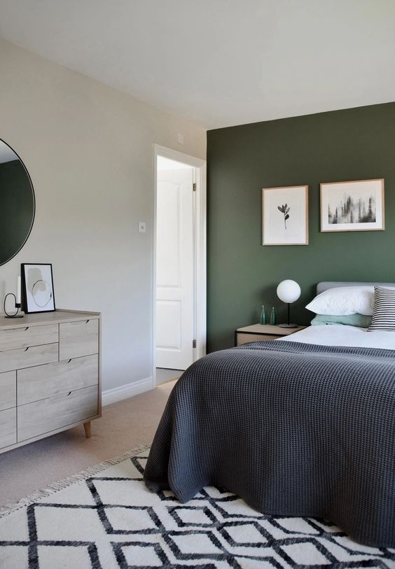 a stylish modern bedroom with a dark green accent wall, a grey bed with bold bedding, a printed rug and a stained sideboard plus a mini gallery wall