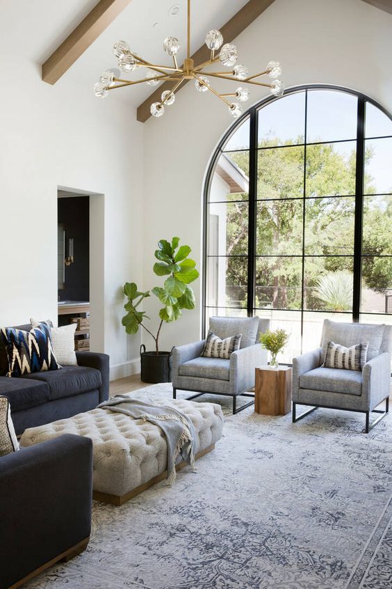 a stylish modern living room with graphite grey and creamy furniture, wooden beams and an arched window with a view of the garden