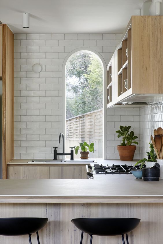 a stylish neutral kitchen with whitewashed cabients, a narrow arched window, a black faucet and black stools