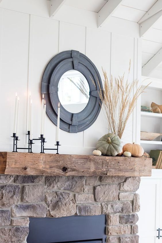 a stylish rustic fall mantel with a black candelabra with tall candles, natural heirloom pumpkins and wheat in a vase plus a mirror in a cool black frame