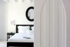 a totally white space with a black bed, mirror and nightstands and an arched pocket door that looks both modern and antique at the same time