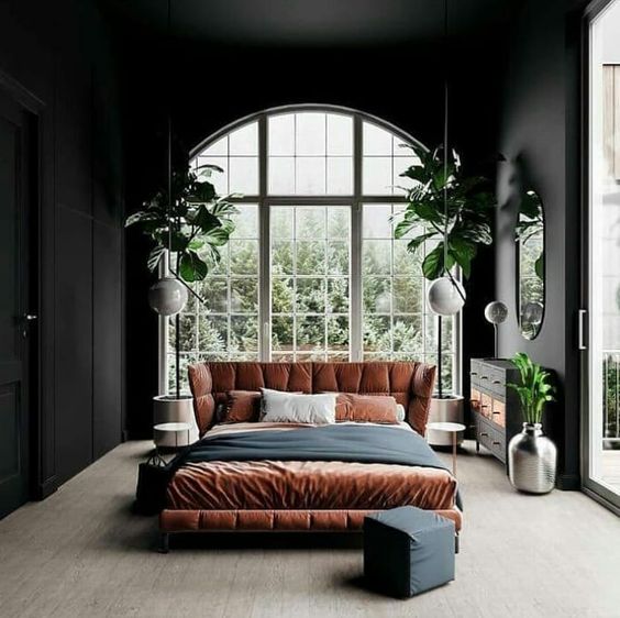 a trendy boho bedroom done in neutrals, black, rust and greenery with an arched window that takes the whole wall