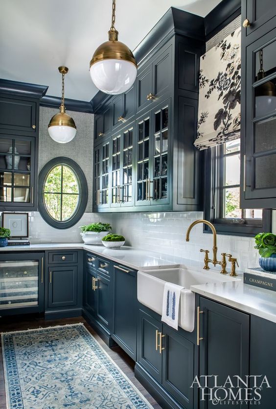 a vintage navy kitchen with shaker cabinets, a white subway tile backsplash and stone countertops, brass pendant lamps, fixtures, handles
