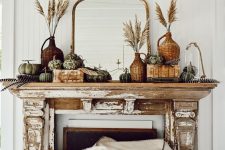 a vintage rustic fall mantel with wheat in woven bottles, heirloom and faux pumpkins, books and a mirror in an ornated frame is chic