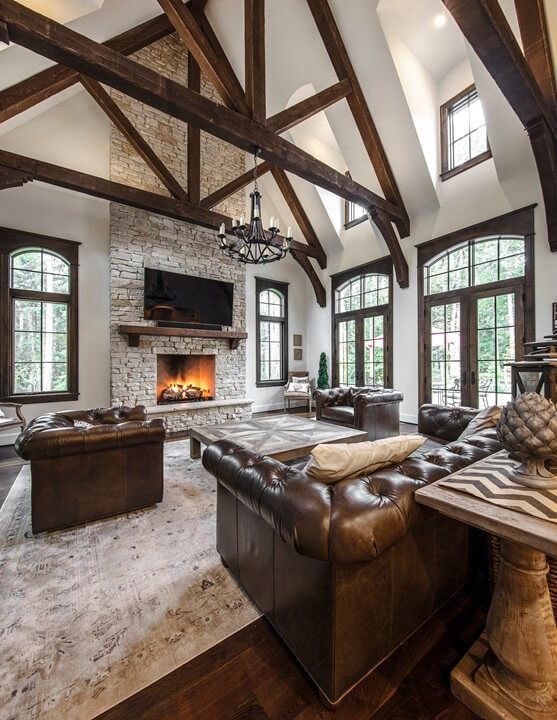 a vintage rustic living room with dark stained wooden beams, brown leather sofas, a large fireplace clad with stone, a large chandelier of metal