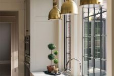 a vintage tan kitchen with white stone countertops, windows instead of a backsplash, brass vintage pendant lamps and topiaries is wow
