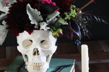 a white skull vase with deep purple blooms, pale leaves, burgundy flowers and berries is a bold and statement-like idea for Halloween