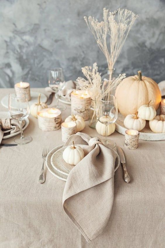 an all-neutral rustic Thanksgiving tablescape with neutral napkins, a tablecloth, pumpkins, wood cuts and dried blooms