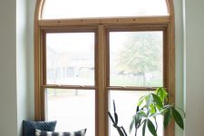 an arched window in a wooden frame, with a matching wooden windowsill and Roman shades over it to have some privayc