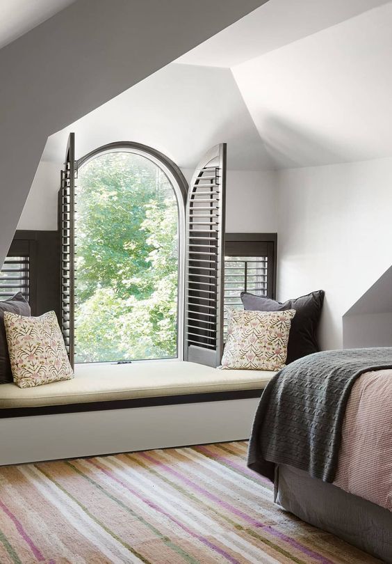an attic bedroom with a small arched window that adds chic to the space and makes it inviting
