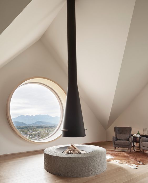 an attic chalet space with an open fireplace, grey chairs and a large porthole window that provides amazing views