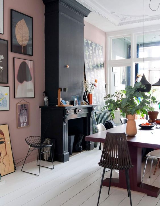 an eclectic dining room with a pink accent wall, a black fireplace, a purple dining table, dark chairs, a cool gallery wall and pendant lamps