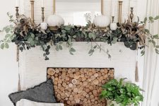 an elegant rustic fall mantel with greenery, white pumpkins, brass candlesticks and a mirror, a wood slice screen in the fireplace is chic