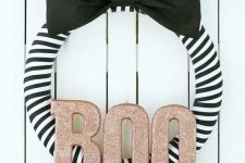 an elegant striped black and white Halloween wreath with a black bow and glitter letters is a very chic idea