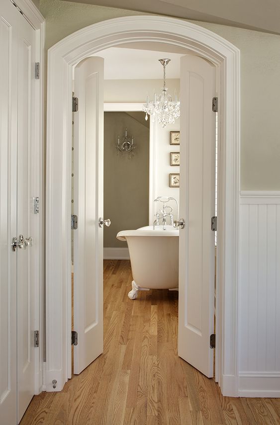 an entrance to a vintage neutral bathroom styled with arched white doors that highlight the style and make the space more chic