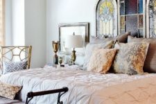 an exquisite bedroom done with vintage wrought furniture, a bed with various chic bedding and stained glass panel headboard for more chic
