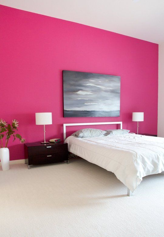 an extra bold bedroom with a hot pink accent wall, a metal bed with white bedding, black nightstands with table lamps and a moody artwork