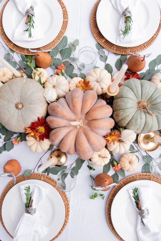 an organic Thanksgiving tablescape with heirloom pumpkins, greenery and bold blooms, woven placemats and white candles and napkins