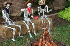 an outdoor Halloween scene with skeletons sitting around the fire made of branches and lights is a cool idea for your outdoor space