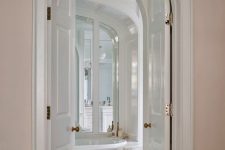 double-height arched doors leading to a refined white bathroom make it look super chic and super cool at the same time