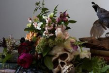 fresh bold blooms paired with a skull and greenery and grapes plus books for refined and chic Halloween decor with a decadent feel