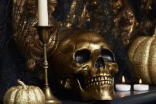 glam black and gold Halloween decor with gold glitter pumpkins, a gold skull, gold candlesticks and white candles, faux black blooms