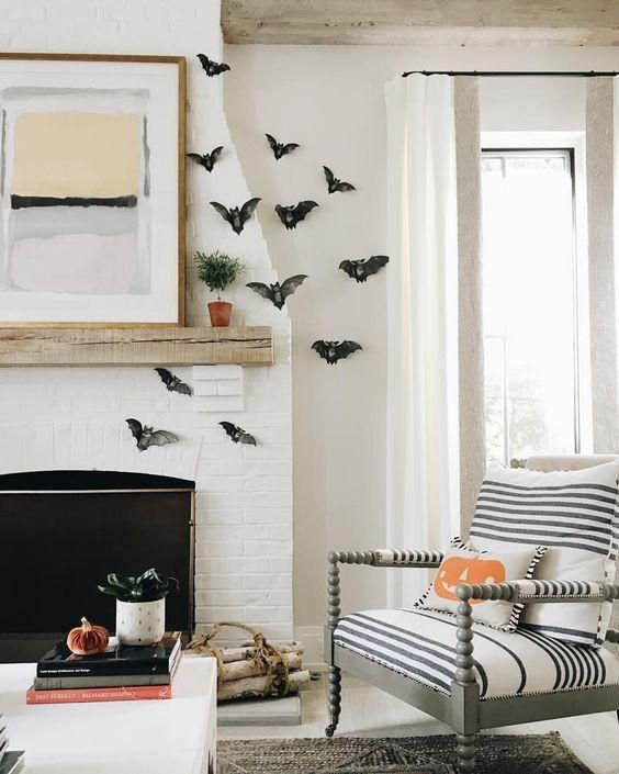 large black paper bats attached to the wall and fireplace plus a jack-o-lantern pillow for modern Halloween decor