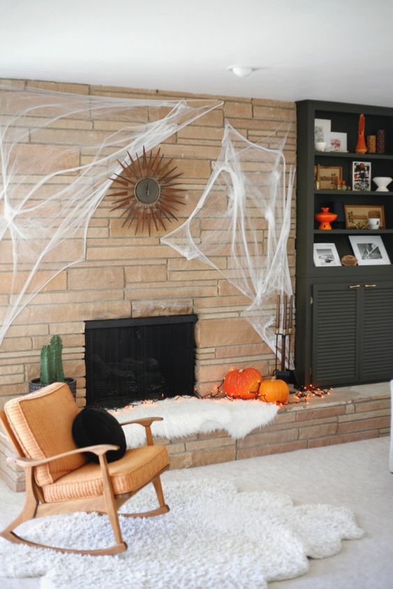 modern Halloween decor done with pumpkins and lights next to the fireplace, with spider web and a black pillow is simple and stylish