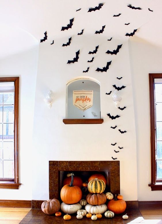modern Halloween decor with a fireplace filled with pumpkins and black paper bats is a lovely idea for the flal