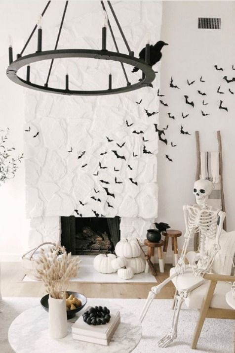 modern Halloween decor with black paper bats, white pumpkins stacked, a skeleton in a rocker, a black chandelier with a blackbird and some wheat