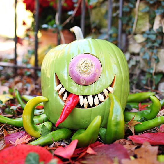 a bold and scary carved green pumpkin with a single eye, some peppers as legs and eating a red pepper is a fun idea for Halloween