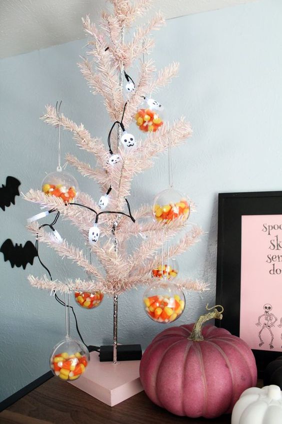 a blush Halloween tree decorated with skulls and with clear Halloween ornaments filled with corn candies