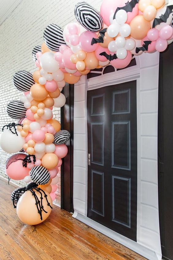 a pink, orange, yellow and striped balloon garland with giant spiders and bats is a gorgeous solution for Halloween