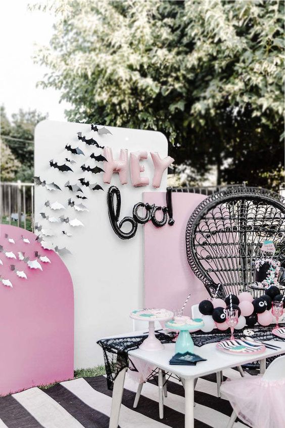 a pink, black and white Halloween party setting with paper bats, balloon letters and a black lace spiderweb runner
