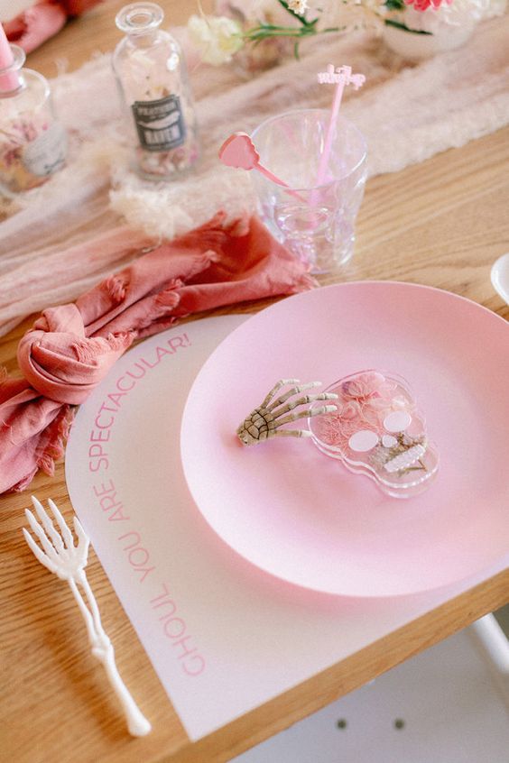 a pretty pink Halloween tablescape with a blush runner and a coral napkin, a pink plate and a skull and a skeleton hand is amazing