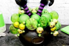 30 a witch cauldron with neon green and gold ornaments and witch’s legs is a cool and easy decoration for Halloween to DIY