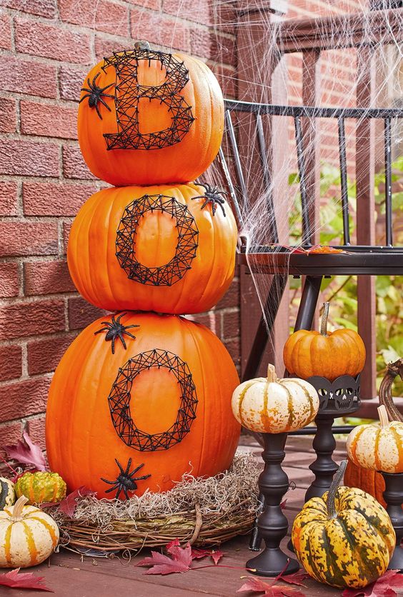 naturally orange stacked pumpkins decorated with nails and yarn, with black spiders are amazing for rustic Halloween styling