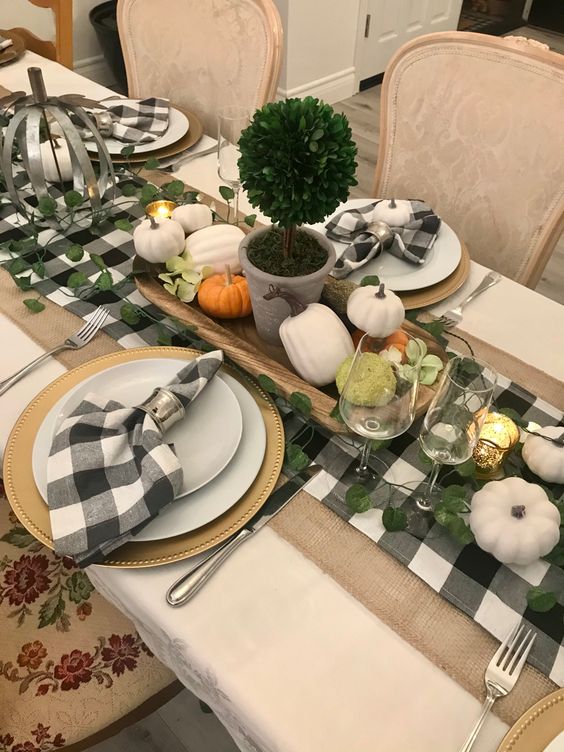 a Thanksgiving tablescape with a buffalo check runner and napkins, greenery and gourds, a topiary and gilded chargers
