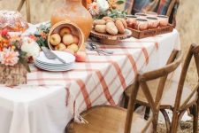 a beautiful fall Thanksgiving tablescape with a plaid runner, bold blooms in terracotta vases, apples and fresh donuts and cider